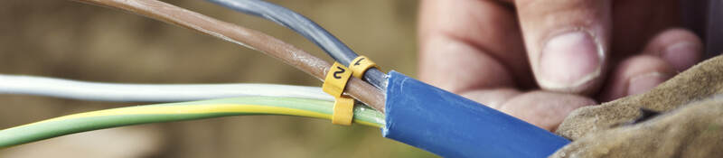 A close-up of a man’s hand holding a cable with exposed wiring. 