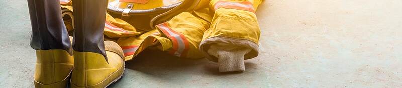 A yellow fireman’s uniform and boots laying on the ground. 