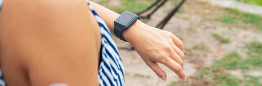 Young woman with wearable patch on arm checking a smartwatch to see her blood sugar level.