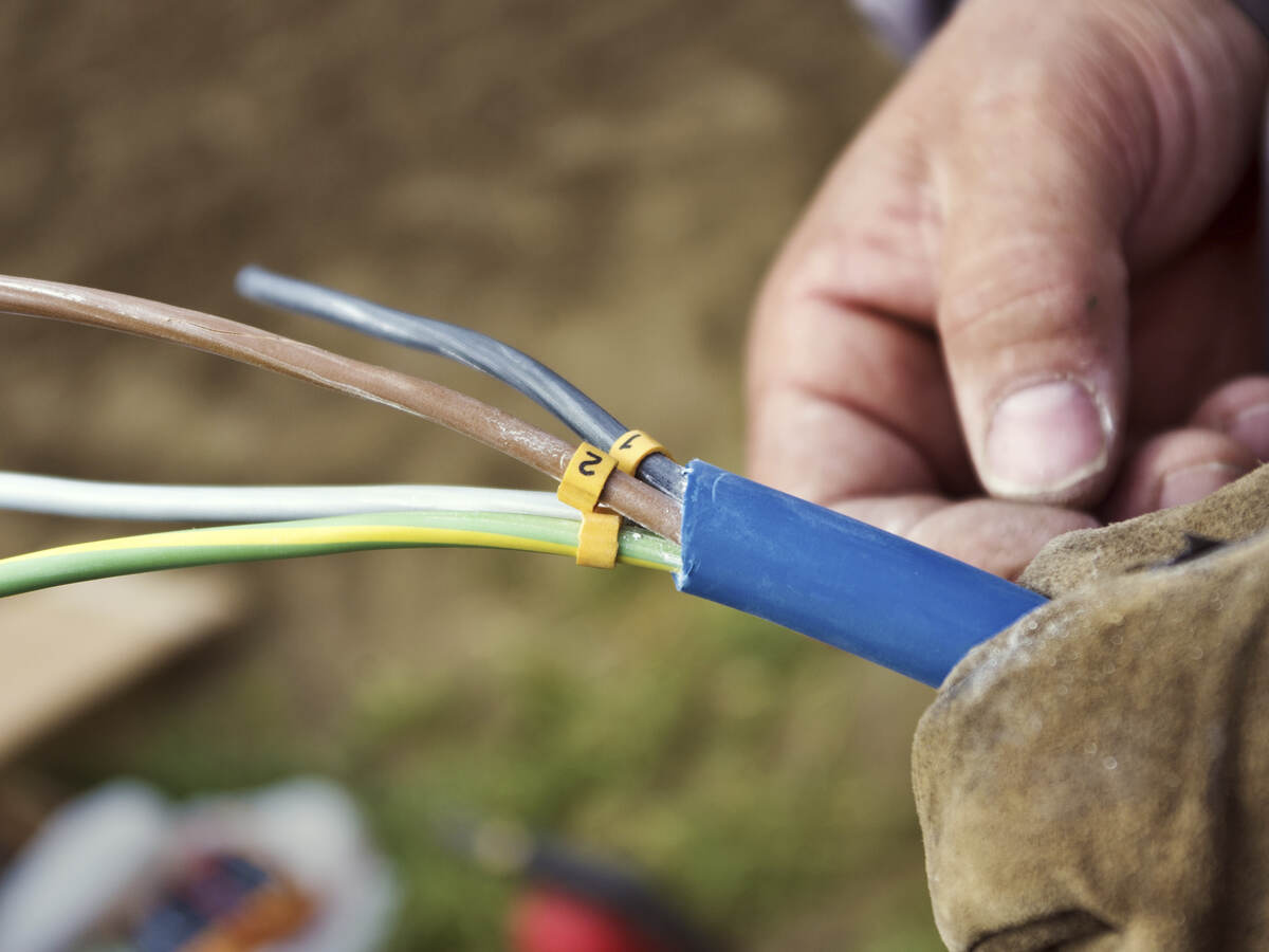 A close-up of a man’s hand holding a cable with exposed wiring. 