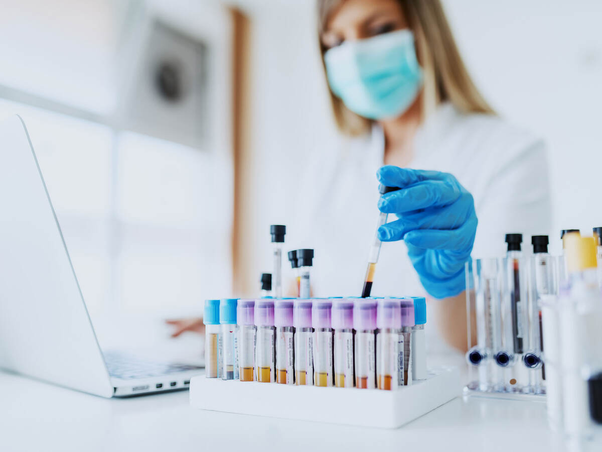 Laboratory technician working on laptop and handling test tubes