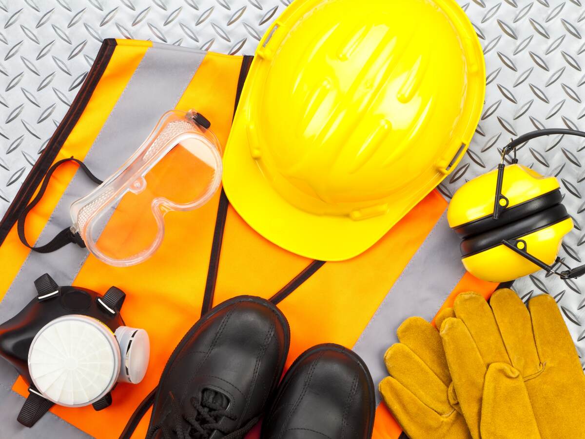 Industrial protective workwear shot from above on diamond-plate background. Includes hard hat, safety glasses, earmuff, gloves, respiratory mask, steel toe shoes and safety vest.