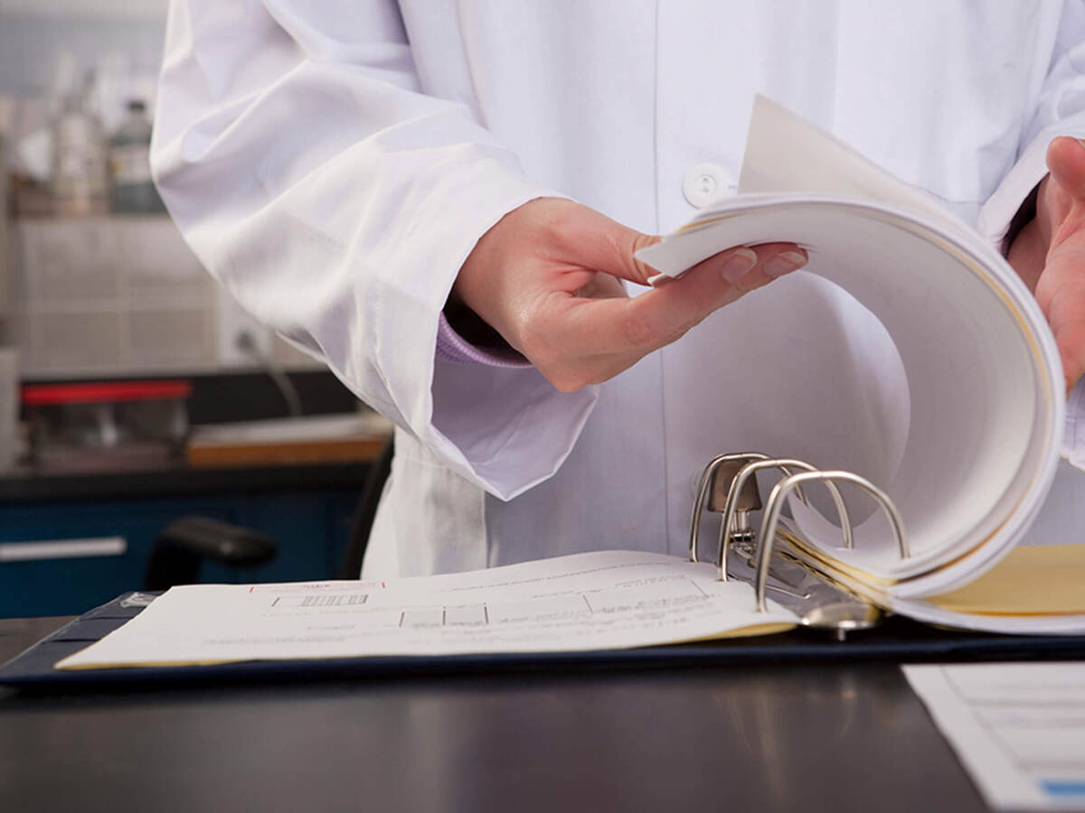 A close up of a lab worker’s hand flipping through three-ring lab binder